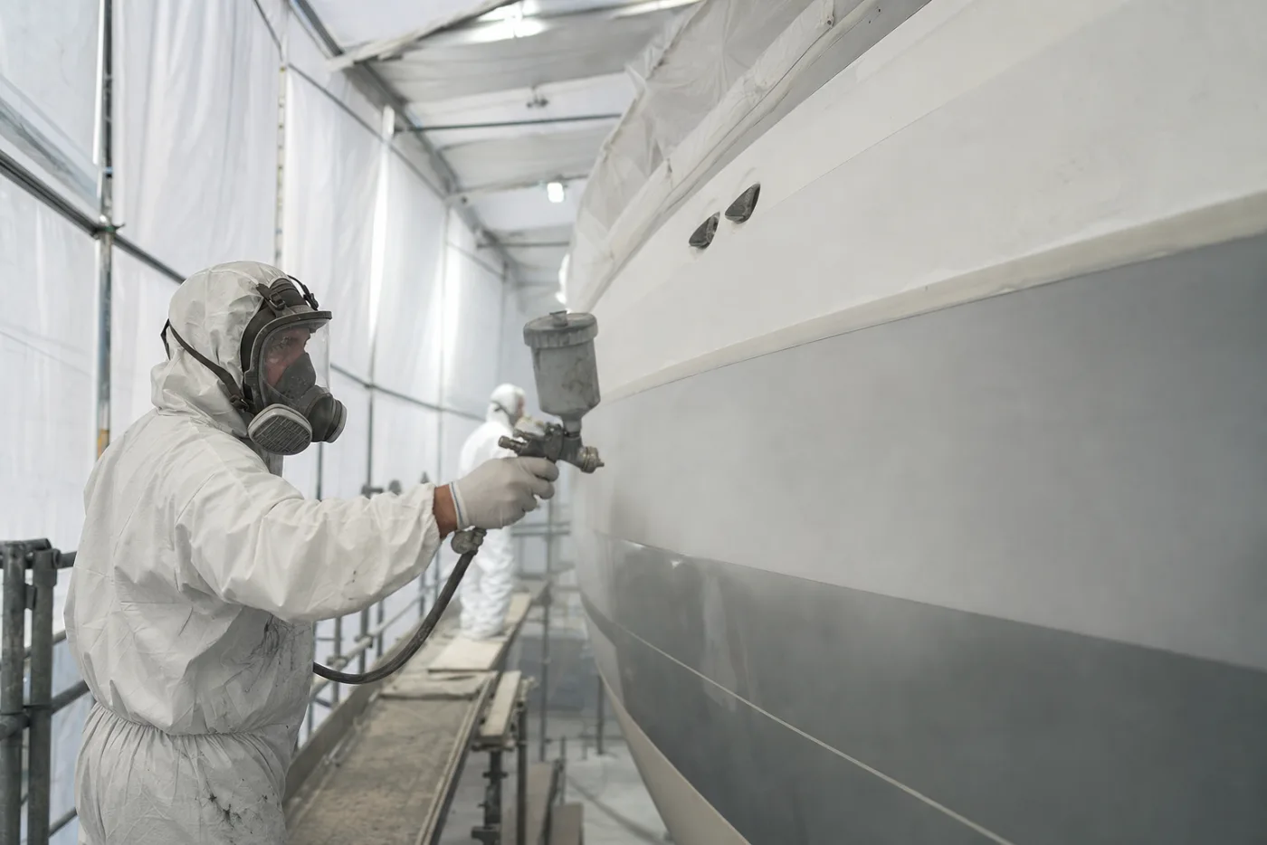 A sprayer in a protective suit working on a tented yacht hull